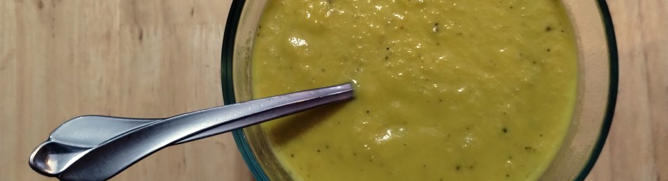 a clear pyrex bowl with yellow cauliflower soup with a spoon